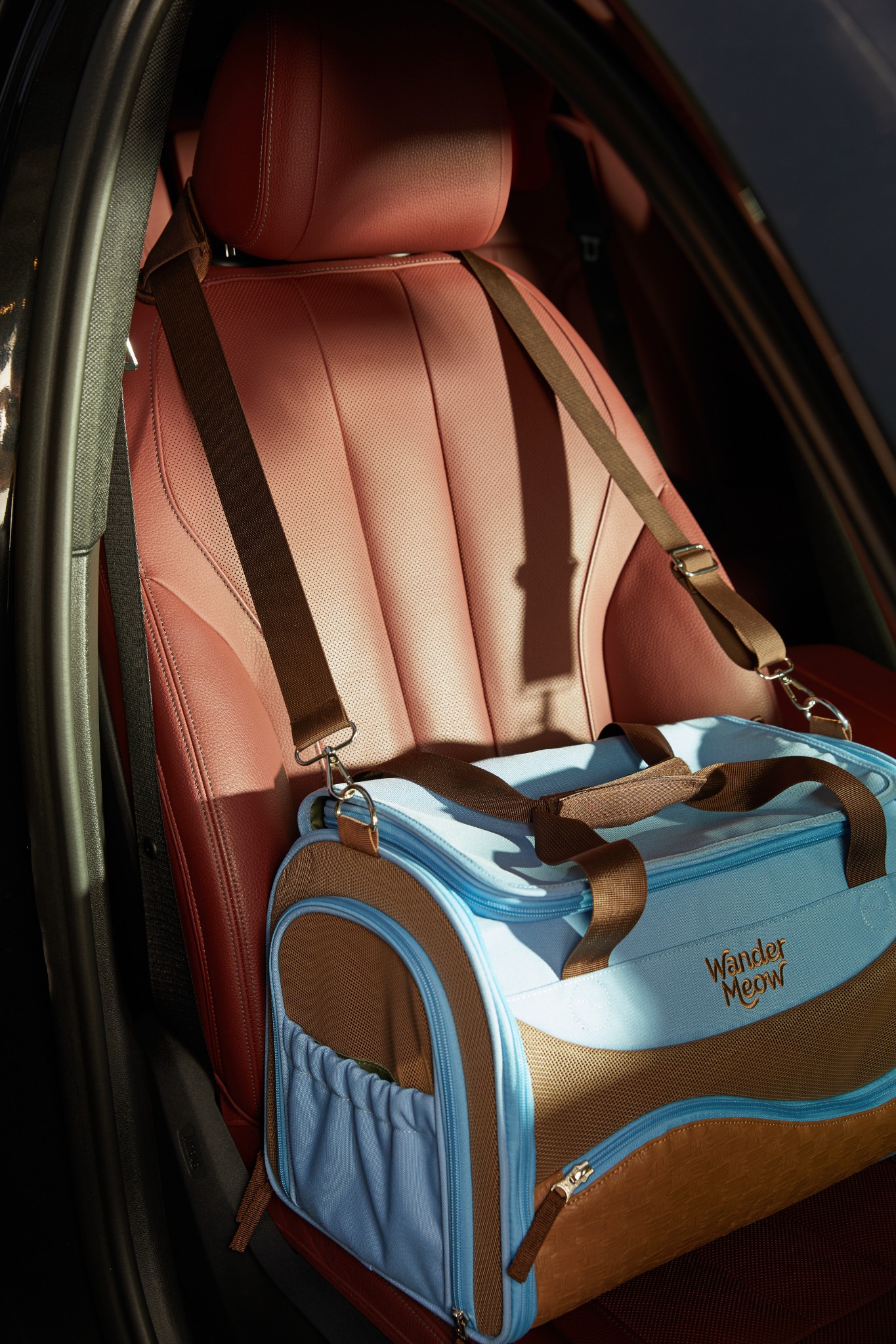 Fully closed blue Wander Meow carrier positioned on a car seat with its shoulder strap in place.
