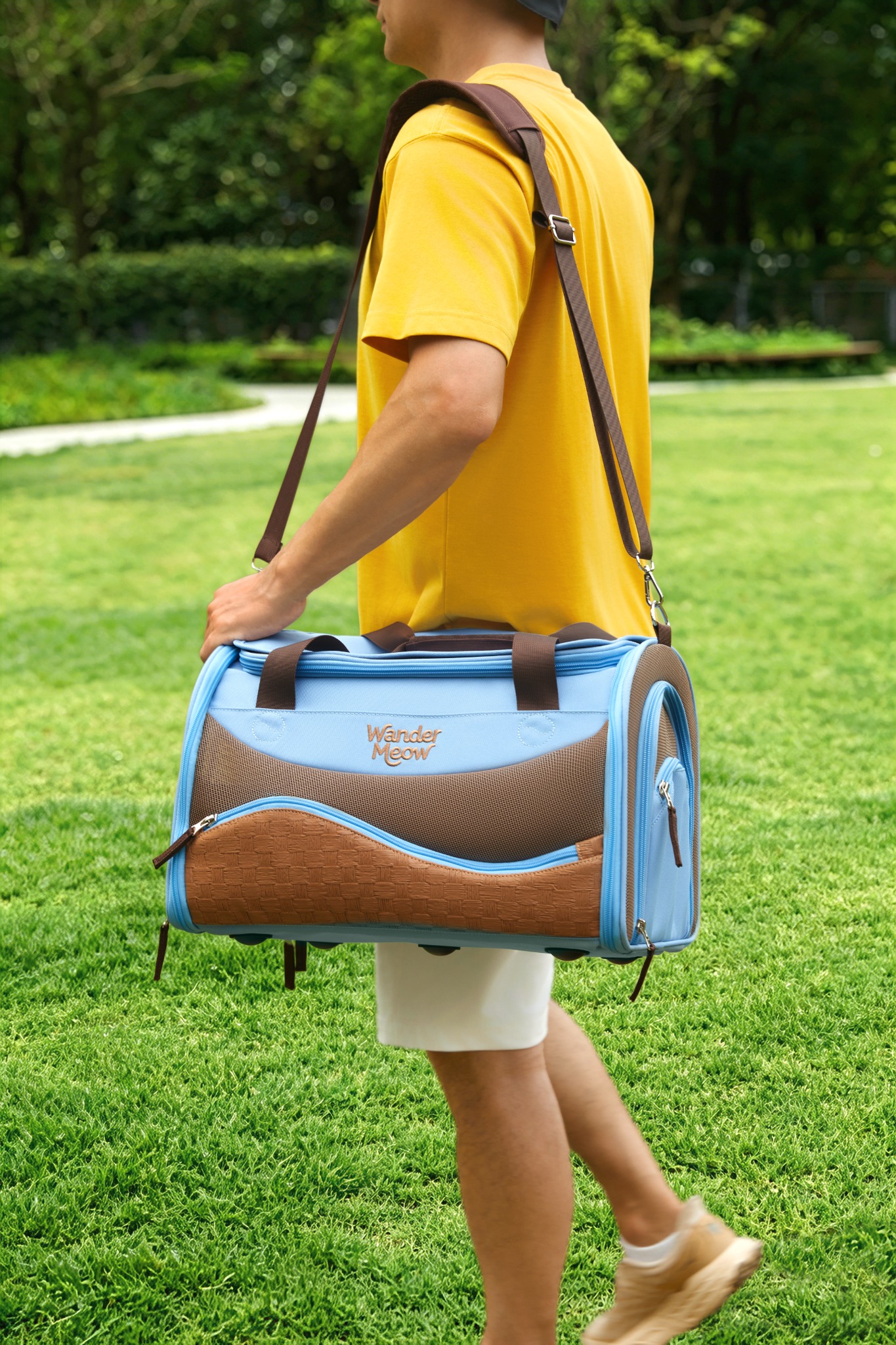 Person carrying the fully closed blue Wander Meow carrier with its shoulder strap outdoors.