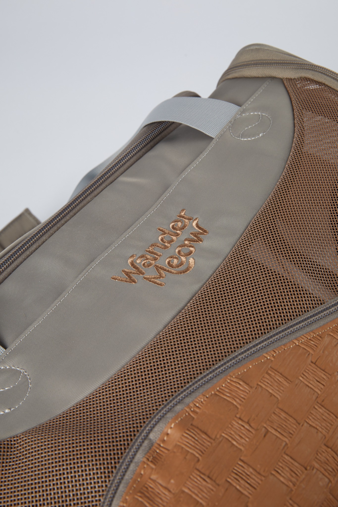 Close view of the original Wander Meow embroidery, gray Oxford fabric, brown mesh, stitching, and zipper on the gray carrier.